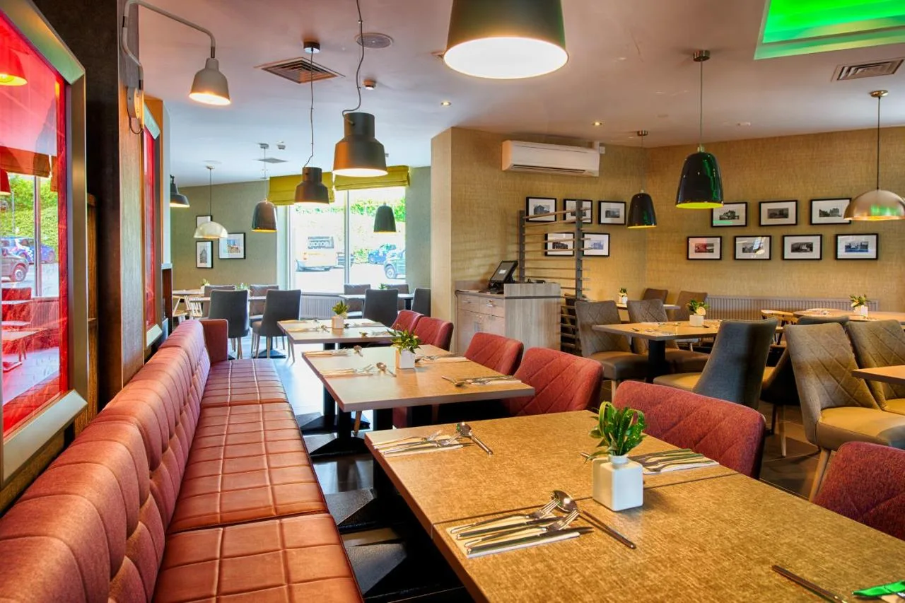 a restaurant with wooden tables and red chairs at Leonardo Hotel Edinburgh Haymarket in Edinburgh